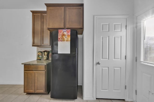 13013 Titanium St, Austin, TX 78754 - kitchen with freestanding refrigerator, stone counters, baseboards, light tile patterned floors, and brown cabinets