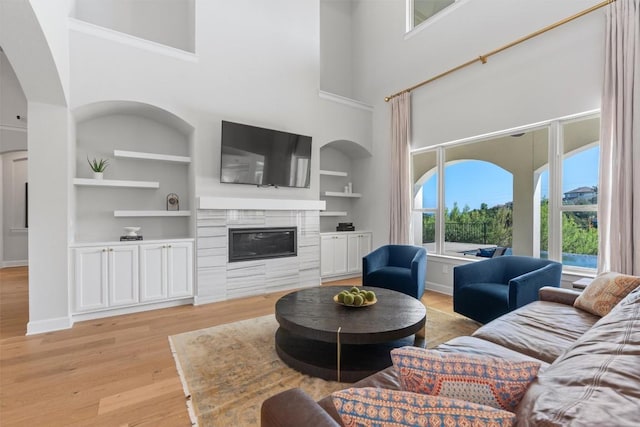 413 Mercer Falls Rd, Lakeway, TX 78738 - living room with light wood-style flooring, a high ceiling, built in shelves, a glass covered fireplace, and arched walkways