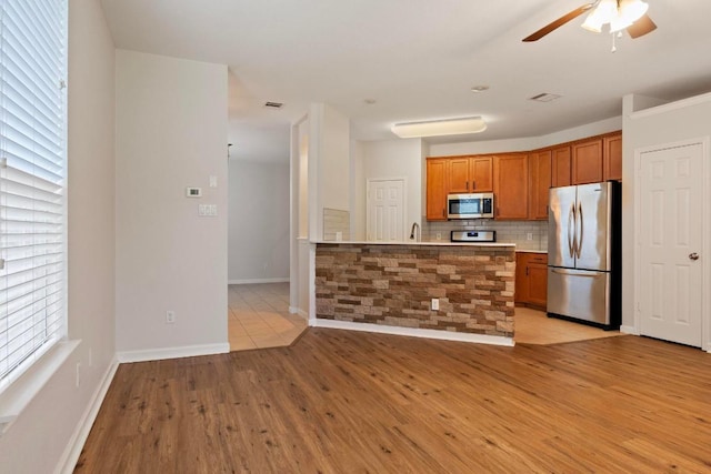 1900 Scofield Ridge Parkway Unit 1703, Austin, TX 78727 - kitchen featuring stainless steel appliances, brown cabinets, a ceiling fan, tasteful backsplash, and light wood finished floors