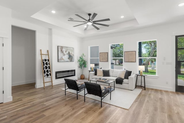 147 Puu Waa Waa Ln, Bastrop, TX 78602 - living area featuring a raised ceiling, light wood finished floors, ceiling fan, recessed lighting, and a glass covered fireplace