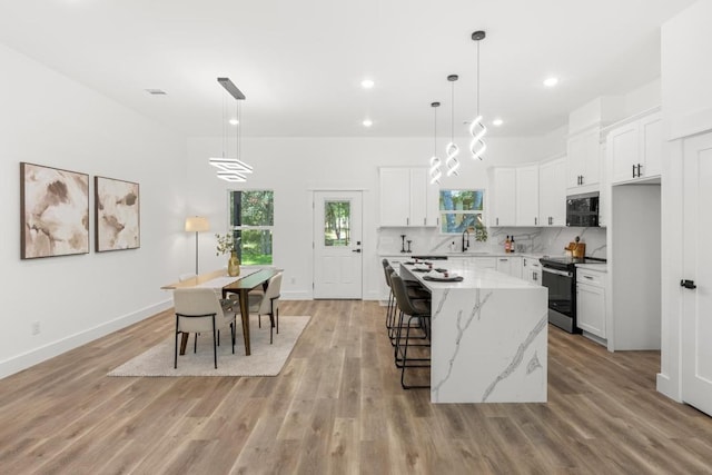 147 Puu Waa Waa Ln, Bastrop, TX 78602 - kitchen with stainless steel range with electric stovetop, a center island, white cabinetry, light wood-type flooring, and light stone countertops