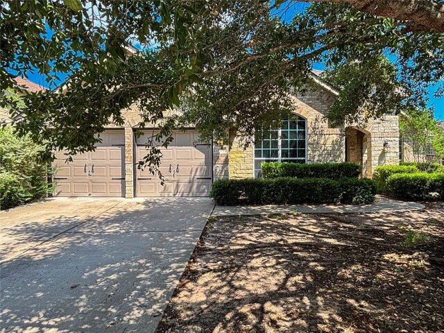 11708 Pillion Pl, Manor, TX 78653 - view of property hidden behind natural elements with stone siding, concrete driveway, and an attached garage