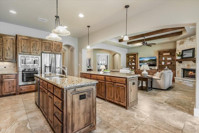 313 Aldea Cv, Georgetown, TX 78633 - kitchen featuring stainless steel appliances, arched walkways, an island with sink, a ceiling fan, and a fireplace