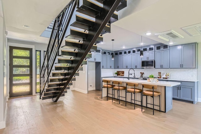 4803 Philco Dr, Austin, TX 78745 - kitchen with light wood-style flooring, light countertops, decorative backsplash, stainless steel microwave, and glass insert cabinets