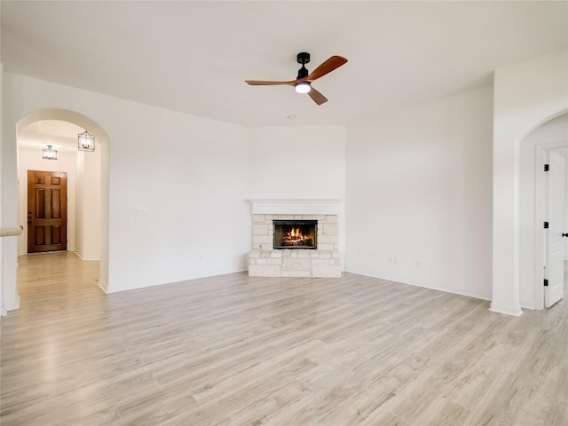 15701 Sayan Cv, Bee Cave, TX 78738 - unfurnished living room featuring a ceiling fan, light wood-type flooring, arched walkways, and a stone fireplace