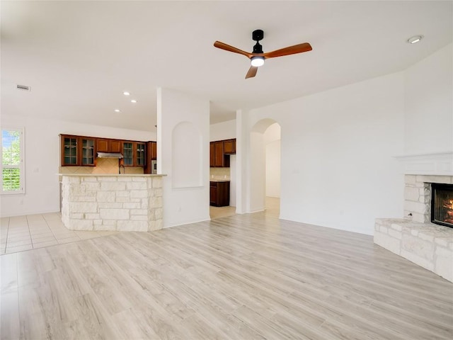 15701 Sayan Cv, Bee Cave, TX 78738 - unfurnished living room featuring arched walkways, a stone fireplace, a ceiling fan, light wood-style floors, and recessed lighting
