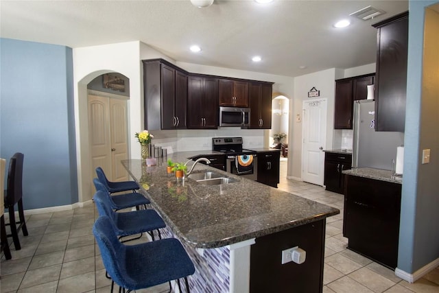 19108 Obed River Dr, Pflugerville, TX 78660 - kitchen featuring appliances with stainless steel finishes, arched walkways, a kitchen breakfast bar, light tile patterned flooring, and tasteful backsplash