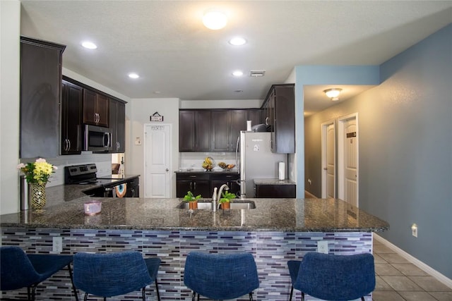 19108 Obed River Dr, Pflugerville, TX 78660 - kitchen featuring appliances with stainless steel finishes, a sink, dark brown cabinetry, light tile patterned floors, and recessed lighting