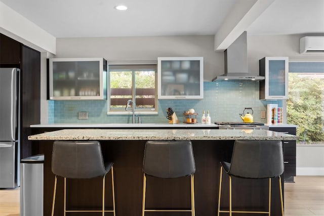 1707 Collier St, Austin, TX 78704 - kitchen featuring freestanding refrigerator, wall chimney exhaust hood, a wall unit AC, a breakfast bar area, and healthy amount of natural light