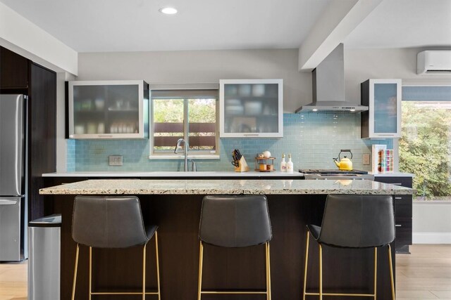 1707 Collier St, Austin, TX 78704 - kitchen featuring freestanding refrigerator, wall chimney range hood, a wall unit AC, a breakfast bar, and backsplash