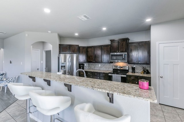 7002 Spirit Of The W Dr, Killeen, TX 76549 - kitchen featuring stainless steel appliances, arched walkways, a kitchen breakfast bar, dark brown cabinetry, and recessed lighting