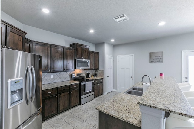 7002 Spirit Of The W Dr, Killeen, TX 76549 - kitchen with appliances with stainless steel finishes, a kitchen bar, backsplash, dark brown cabinetry, and light tile patterned floors
