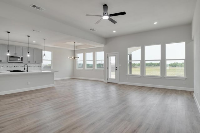 203 Alonzo Dr, Del Valle, TX 78617 - unfurnished living room featuring recessed lighting, ceiling fan, light wood-style flooring, a chandelier, and a tray ceiling