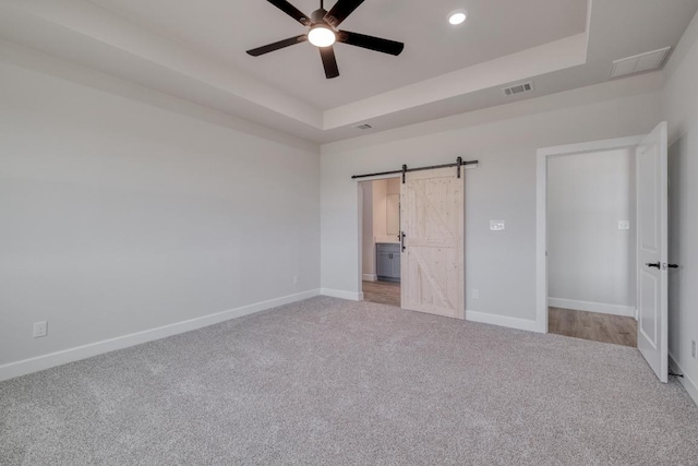 203 Alonzo Dr, Del Valle, TX 78617 - unfurnished bedroom featuring carpet, a raised ceiling, a barn door, recessed lighting, and ensuite bathroom