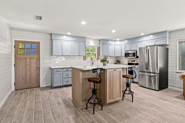 810 River Rd, Wimberley, TX 78676 - kitchen featuring appliances with stainless steel finishes, light countertops, wood finish floors, a kitchen bar, and gray cabinetry
