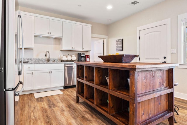 25404 Hamilton Pool Rd, Round Mountain, TX 78663 - kitchen featuring stainless steel appliances, light wood-type flooring, white cabinetry, light stone countertops, and a sink
