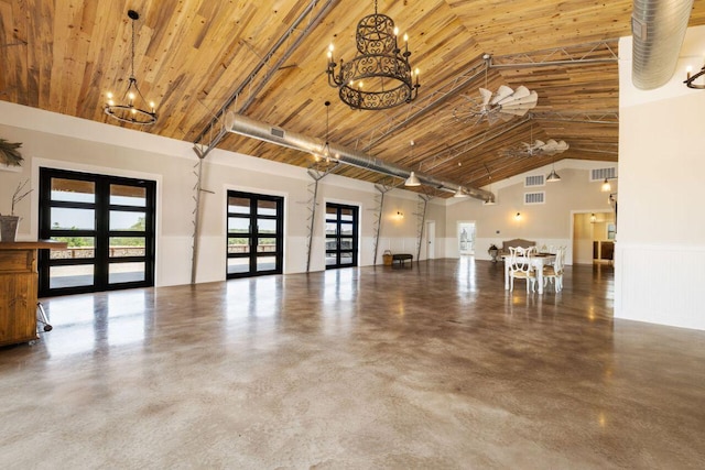 25404 Hamilton Pool Rd, Round Mountain, TX 78663 - unfurnished living room with a chandelier, concrete floors, a wainscoted wall, high vaulted ceiling, and french doors