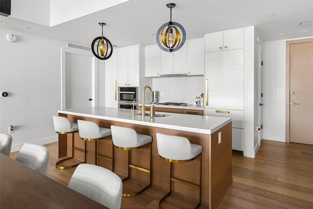 70 Rainey St Unit 2106, Austin, TX 78701 - kitchen featuring hardwood / wood-style floors, light countertops, a breakfast bar area, a center island with sink, and white cabinetry