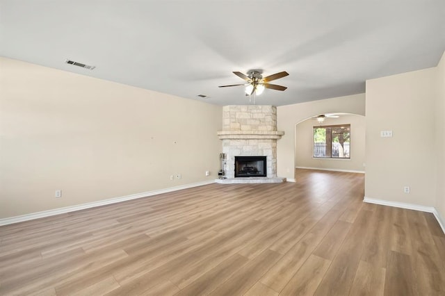 2511 Jacqueline Dr, Leander, TX 78641 - unfurnished living room featuring a ceiling fan, arched walkways, light wood-style floors, baseboards, and a stone fireplace