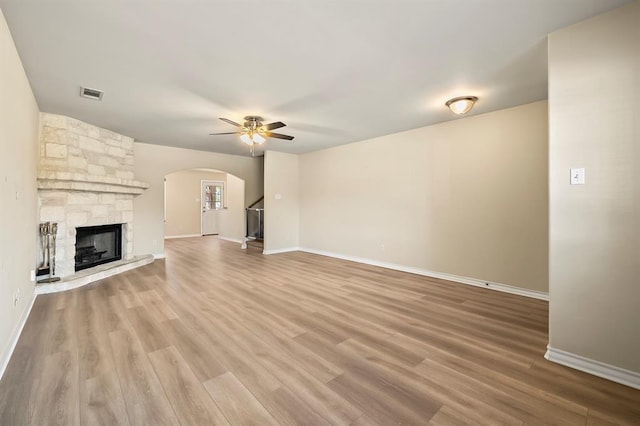 2511 Jacqueline Dr, Leander, TX 78641 - unfurnished living room with ceiling fan, arched walkways, wood finished floors, baseboards, and a stone fireplace
