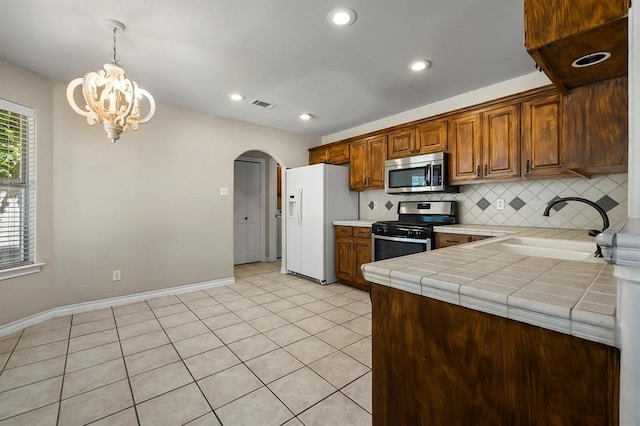 2511 Jacqueline Dr, Leander, TX 78641 - kitchen featuring appliances with stainless steel finishes, a sink, arched walkways, tile countertops, and tasteful backsplash