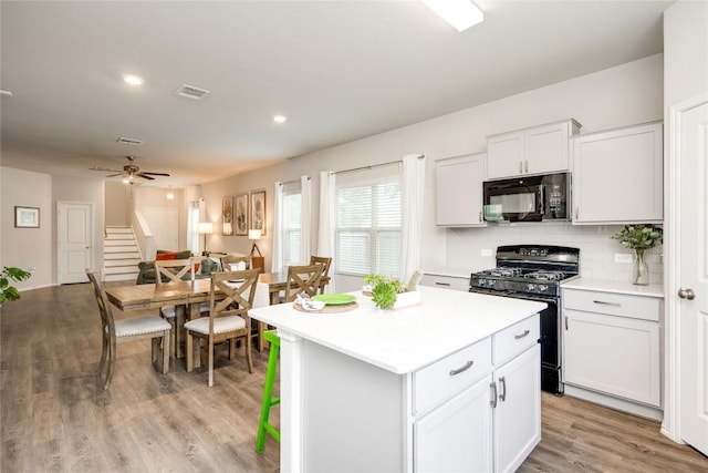 10701 Dimitrios Dr, Austin, TX 78747 - kitchen with black appliances, a center island, light countertops, light wood-style flooring, and white cabinetry