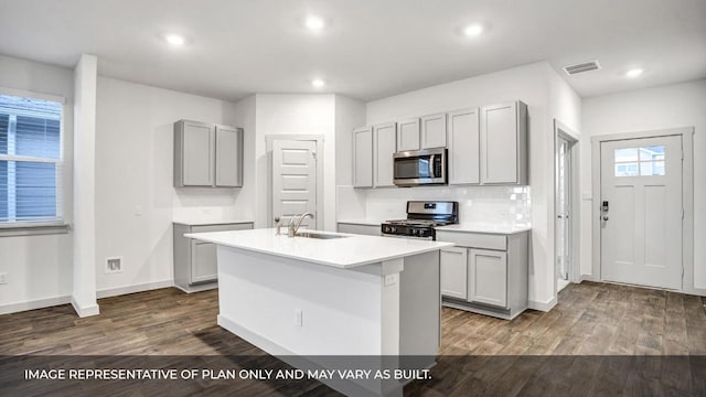 549 Osprey Dr, Leander, TX 78641 - kitchen with stainless steel appliances, a sink, gray cabinets, dark wood-style flooring, and a kitchen island with sink