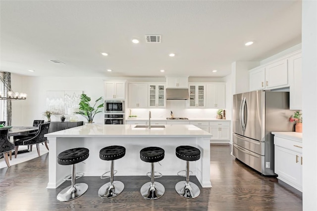 5028 Olimpico Way, Leander, TX 78641 - kitchen featuring stainless steel appliances, dark wood finished floors, a kitchen island with sink, white cabinetry, and glass insert cabinets