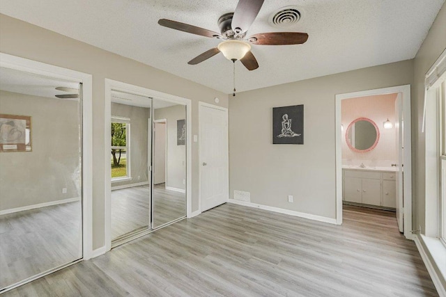 8711 Bridgeport Dr, Austin, TX 78758 - unfurnished bedroom with light wood finished floors, ensuite bathroom, ceiling fan, a textured ceiling, and two closets
