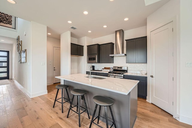 1531 N Red Bud Ln Unit 34, Round Rock, TX 78665 - kitchen featuring wall chimney range hood, appliances with stainless steel finishes, light stone counters, light wood-style flooring, and an island with sink