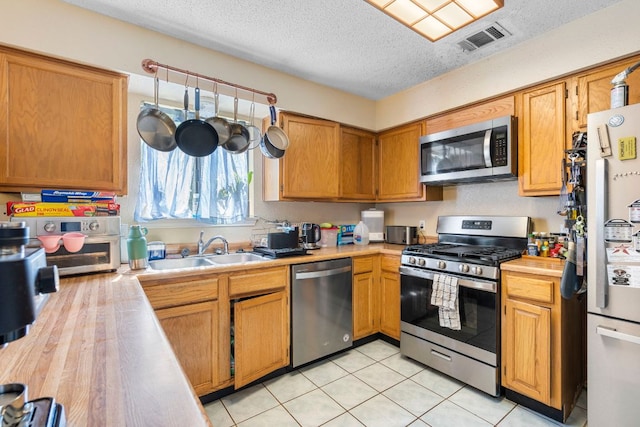 2656 Piping Rock Trl, Austin, TX 78748 - kitchen with appliances with stainless steel finishes, a sink, a textured ceiling, light tile patterned floors, and brown cabinets