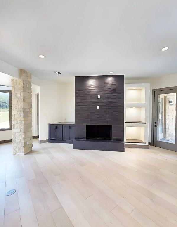 2700 Marina Shores Dr, Spicewood, TX 78669 - unfurnished living room with a fireplace, light wood finished floors, built in shelves, decorative columns, and recessed lighting