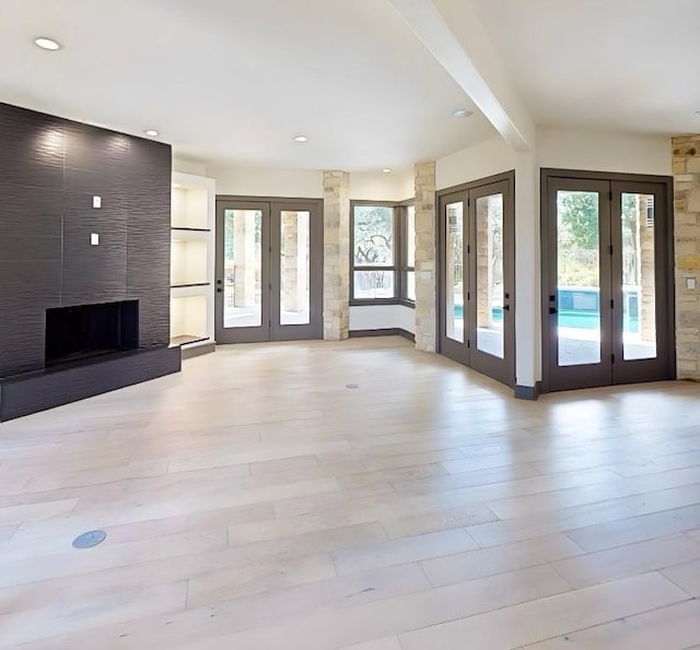 2700 Marina Shores Dr, Spicewood, TX 78669 - unfurnished living room featuring french doors, beam ceiling, light wood-style floors, recessed lighting, and a large fireplace