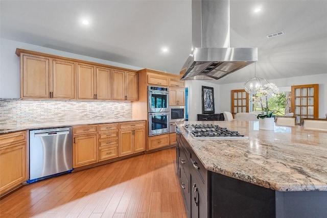 408 Sombrero, Horseshoe Bay, TX 78657 - kitchen featuring appliances with stainless steel finishes, island range hood, a chandelier, tasteful backsplash, and light stone counters