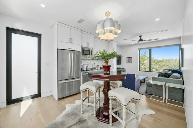 8209 Two Coves Dr, Austin, TX 78730 - kitchen featuring appliances with stainless steel finishes, light wood finished floors, white cabinetry, backsplash, and a ceiling fan