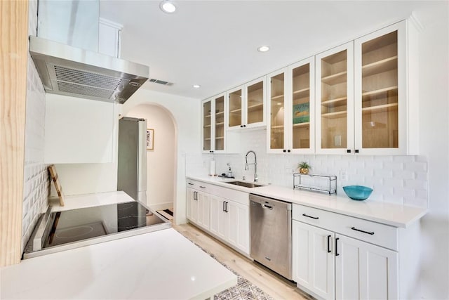 2419 Trail Of The Madrones, Austin, TX 78746 - kitchen with stainless steel appliances, wall chimney range hood, arched walkways, decorative backsplash, and white cabinetry