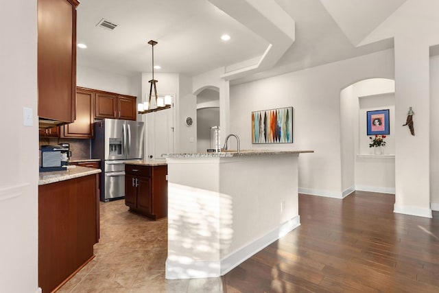114 Fred Couples Dr, Round Rock, TX 78664 - kitchen with stainless steel refrigerator with ice dispenser, an island with sink, arched walkways, light stone countertops, and hanging light fixtures