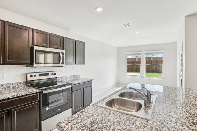9701 Kensley Rose Dr, Killeen, TX 76542 - kitchen featuring stainless steel appliances, a sink, tasteful backsplash, dark brown cabinetry, and light stone countertops
