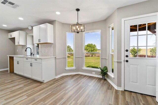 1145 Lago Vista St, San Marcos, TX 78666 - kitchen with light wood finished floors, light countertops, white cabinets, a chandelier, and decorative backsplash