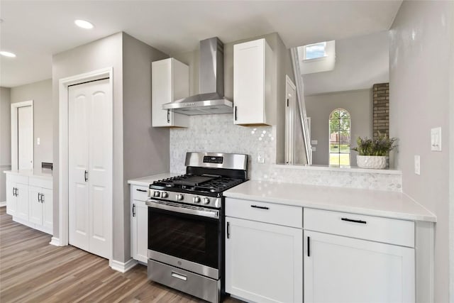 1145 Lago Vista St, San Marcos, TX 78666 - kitchen featuring wall chimney range hood, stainless steel range with gas stovetop, light wood-type flooring, decorative backsplash, and white cabinetry