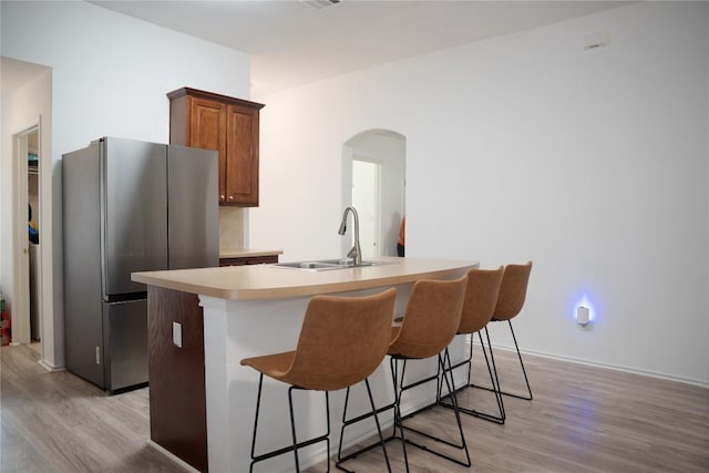 9305 Pioneer Forest Dr, Austin, TX 78744 - kitchen featuring freestanding refrigerator, light wood-type flooring, an island with sink, arched walkways, and a kitchen breakfast bar