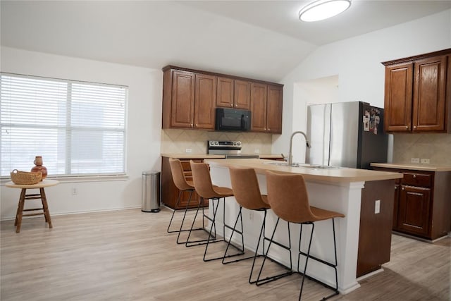 9305 Pioneer Forest Dr, Austin, TX 78744 - kitchen featuring appliances with stainless steel finishes, a kitchen island with sink, a kitchen bar, light countertops, and lofted ceiling