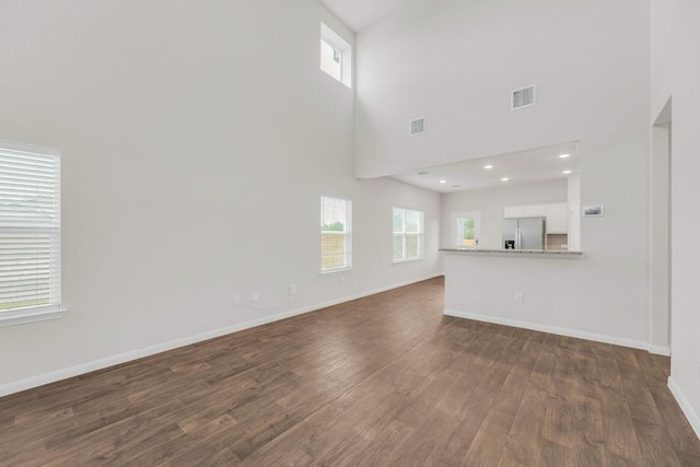 2900 Tweedy Trl, Pflugerville, TX 78660 - unfurnished living room featuring plenty of natural light, dark wood-style flooring, a towering ceiling, and baseboards
