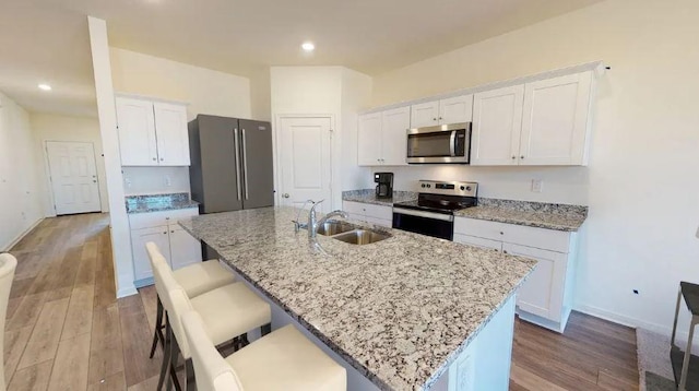 129 Bridgeview Dr, Hutto, TX 78634 - kitchen featuring appliances with stainless steel finishes, a sink, light wood-type flooring, a center island with sink, and white cabinetry