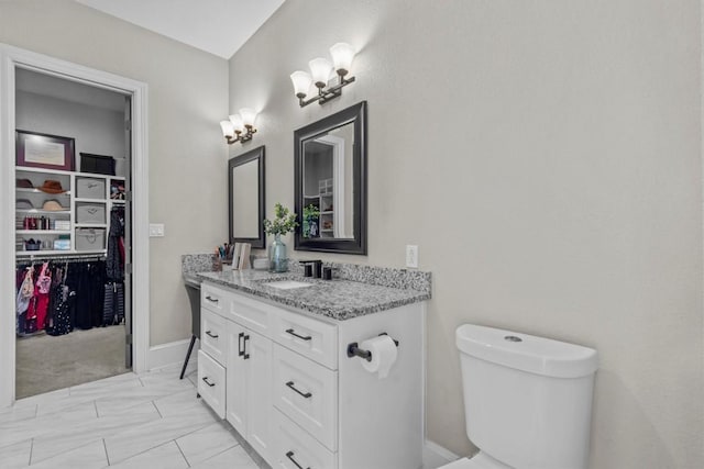 bathroom featuring toilet, vanity, marble look tiles, and a walk in closet