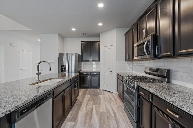 16816 Caperi Dr, Pflugerville, TX 78660 - kitchen with appliances with stainless steel finishes, a sink, light stone counters, light wood-style floors, and recessed lighting