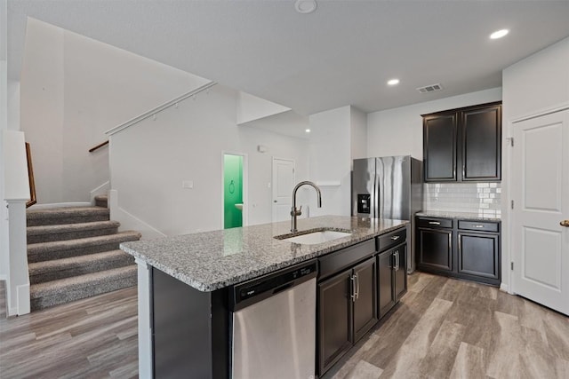 16816 Caperi Dr, Pflugerville, TX 78660 - kitchen with appliances with stainless steel finishes, a sink, light wood-style flooring, light stone countertops, and an island with sink