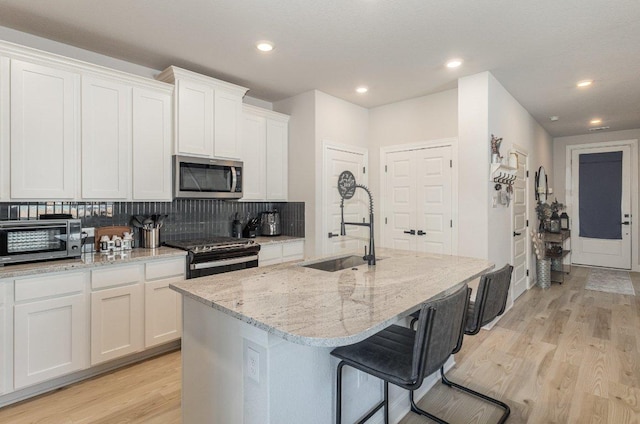 119 Nandina Path, Bastrop, TX 78602 - kitchen featuring stainless steel microwave, black range with gas cooktop, a sink, light wood finished floors, and recessed lighting