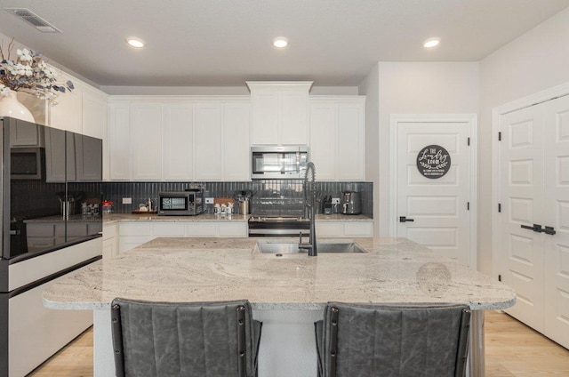 119 Nandina Path, Bastrop, TX 78602 - kitchen featuring appliances with stainless steel finishes, white cabinetry, tasteful backsplash, light wood-style floors, and a center island with sink