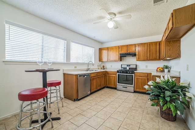 409 Mountain Laurel Dr, Cedar Park, TX 78613 - kitchen featuring appliances with stainless steel finishes, under cabinet range hood, a sink, brown cabinetry, and a textured ceiling